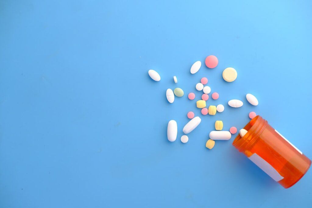 A variety of pills spilled from an orange prescription bottle on a blue surface.