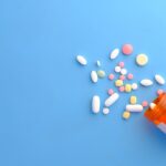 A variety of pills spilled from an orange prescription bottle on a blue surface.